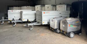 Dichte aanhangwagens en hogedrukreinigers in verschillende maten staan naast elkaar in een opslagruimte.